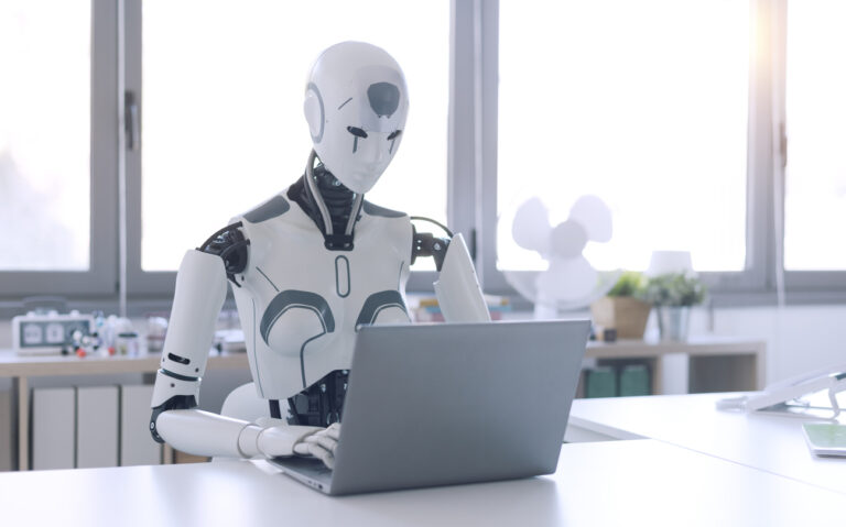 A humanoid robot works in an office on a laptop, showcasing the utility of automation in repetitive and tedious tasks.