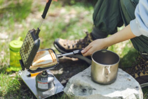 An Asian woman is cooking outside using a gas cylinder. Make hot sandwiches using  a hot sandwich maker.